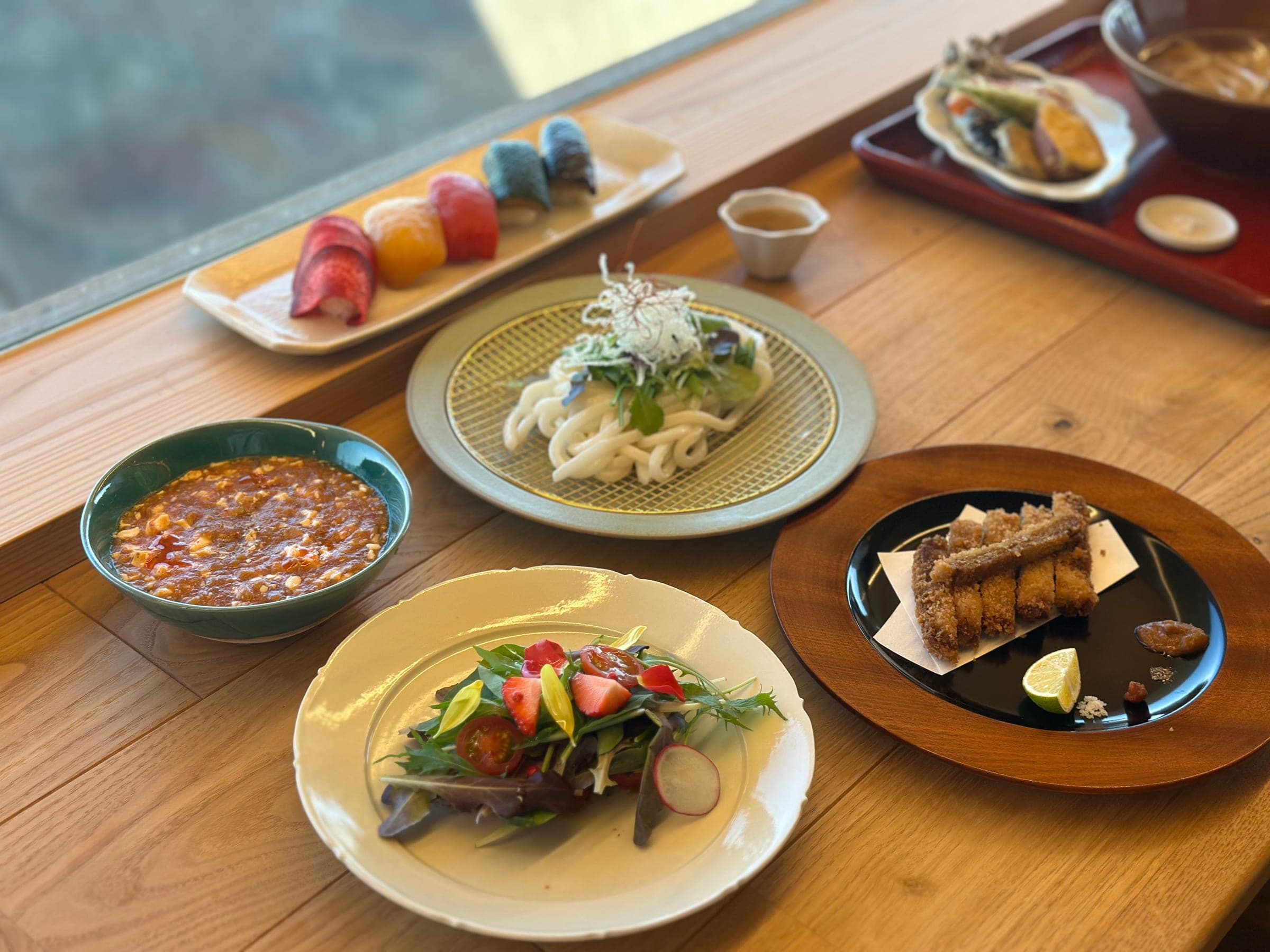 木桌上的一套素食和食：彩色蔬菜壽司、冷烏龍麵、沙拉、炸物和一碗麻婆豆腐